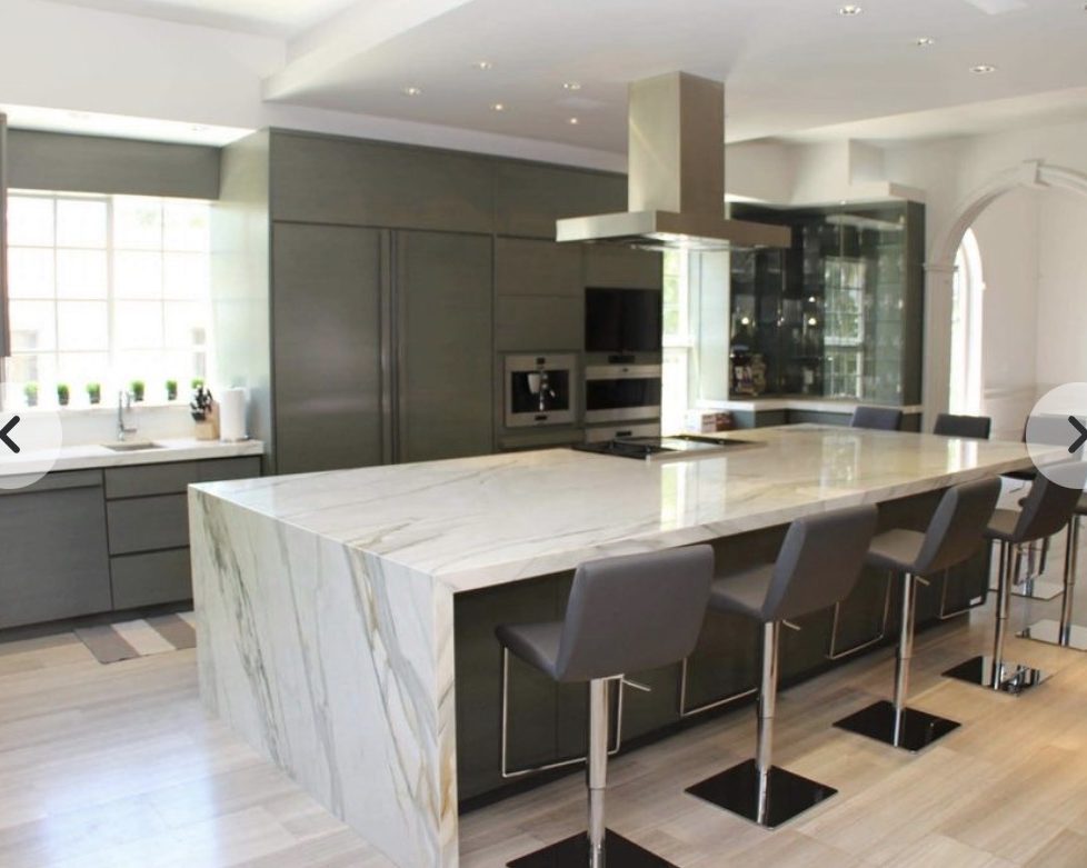 A finished custom kitchen with a waterfall marble island and grey cabinetry
